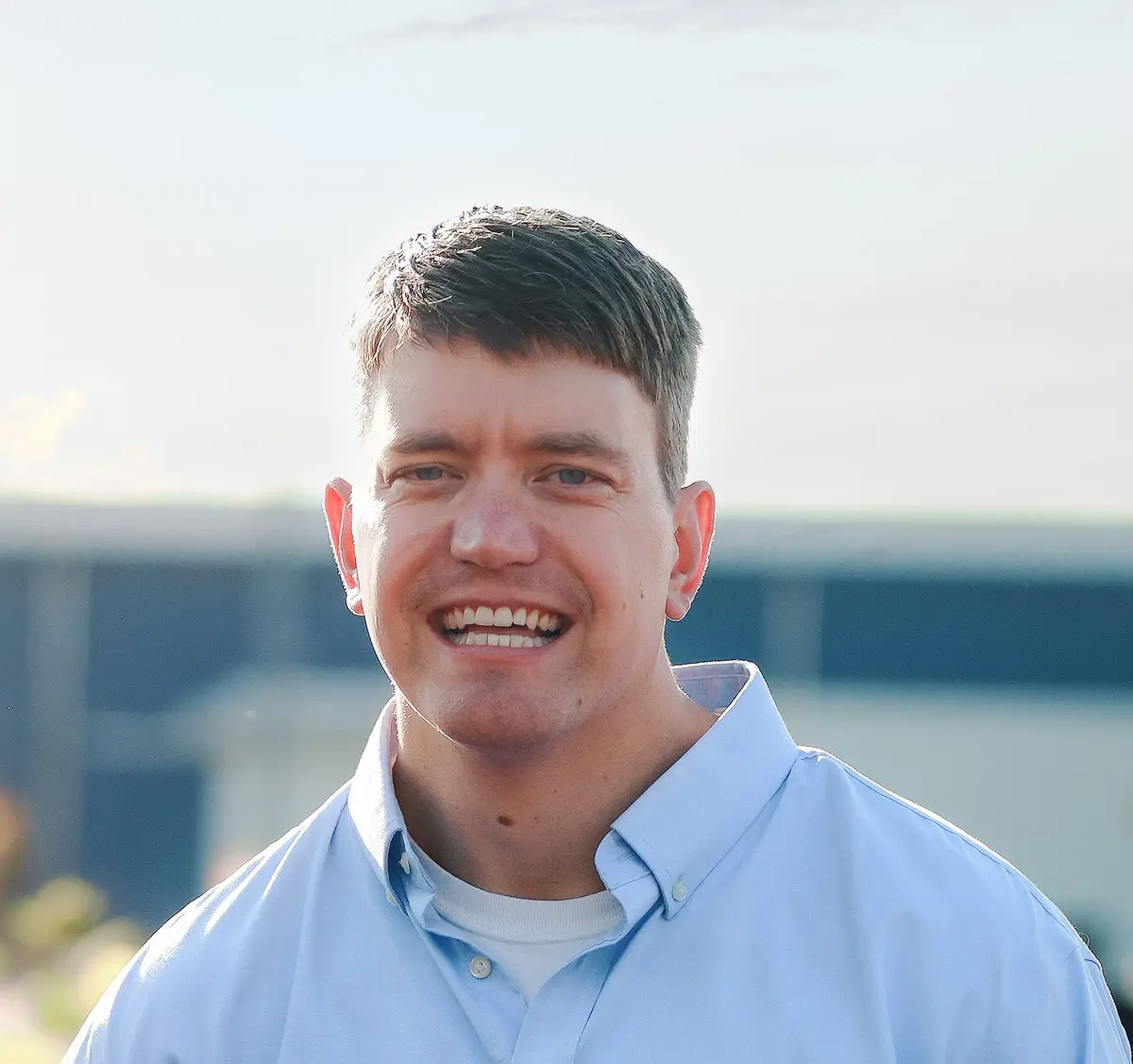 A person outside smiles toward the camera and wears a collared shirt.