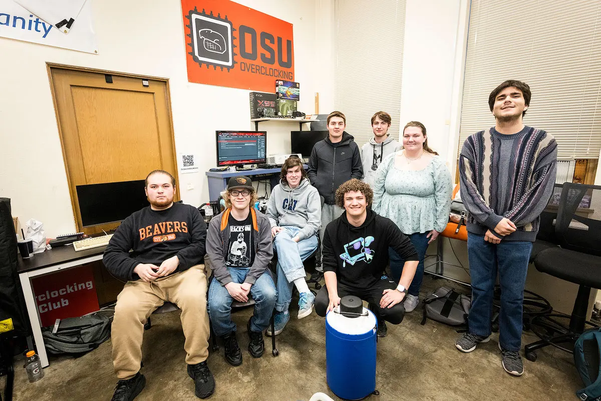 A group of students pose together in a room filled with computer equipment, electronics, and monitors.