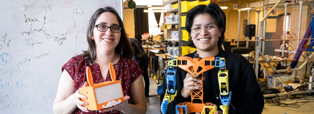 Naomi Fitter alongside an undergraduate student holding up parts of their robot, called SAMI. 