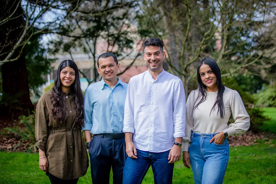 Four people stand outdoors and face toward the camera smiling with grass and vegetation in the background.