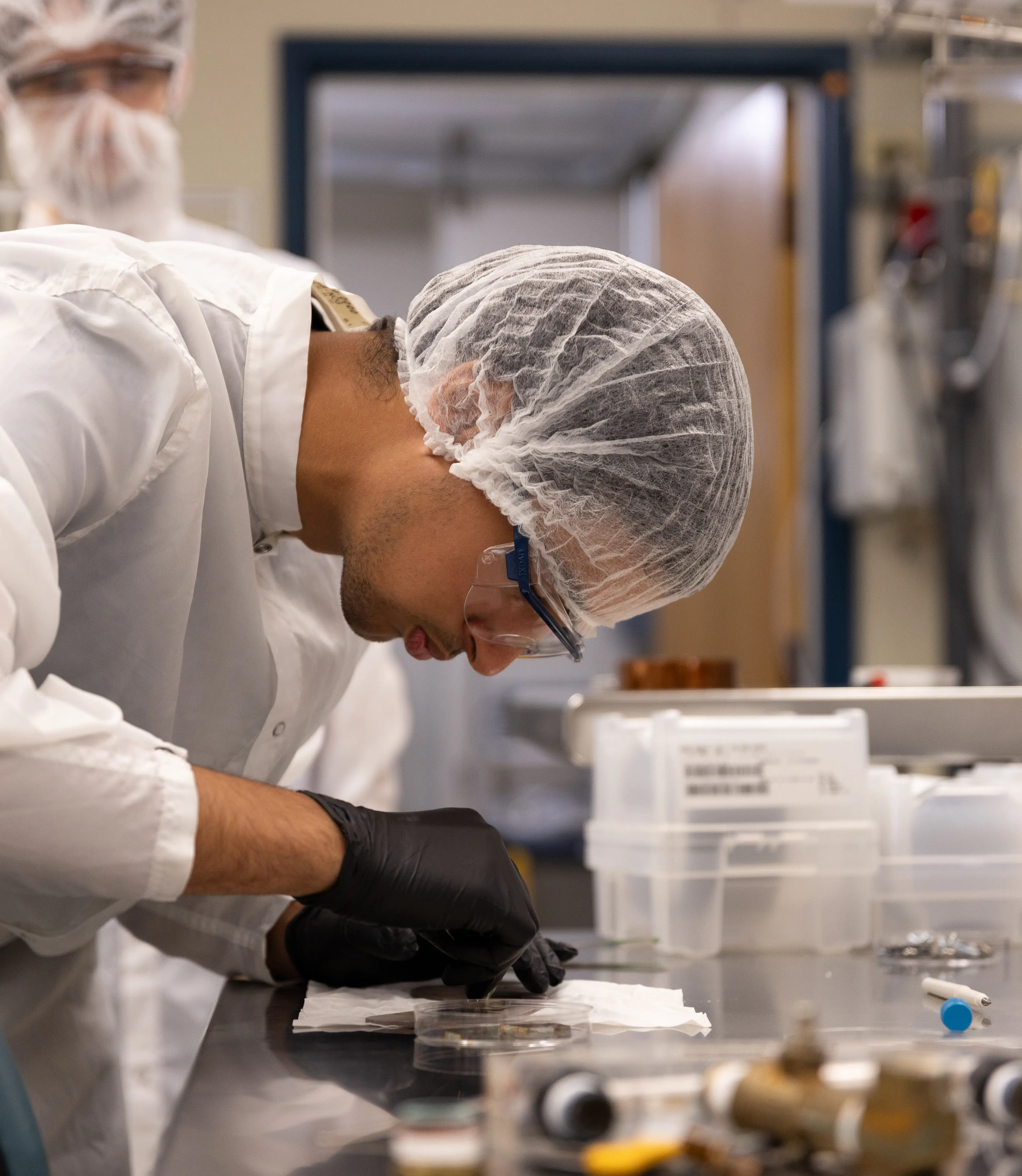 Student researcher wearing white protective gear working on an experiment in a lab.