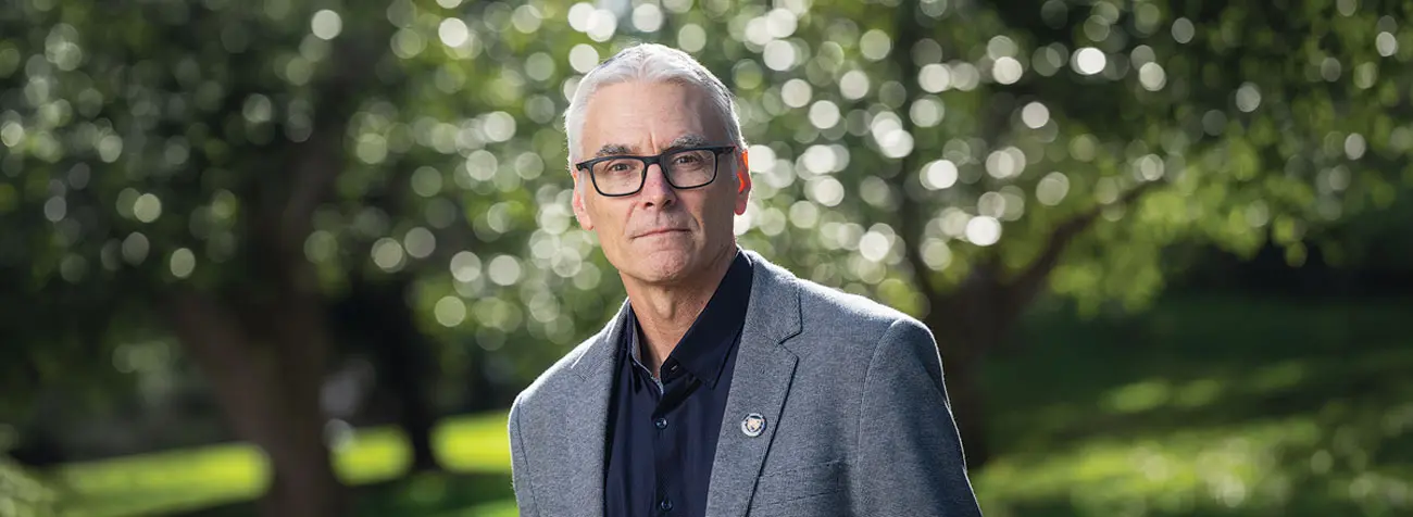 Todd Palmer in glasses and a suit surrounded by green vegetation.