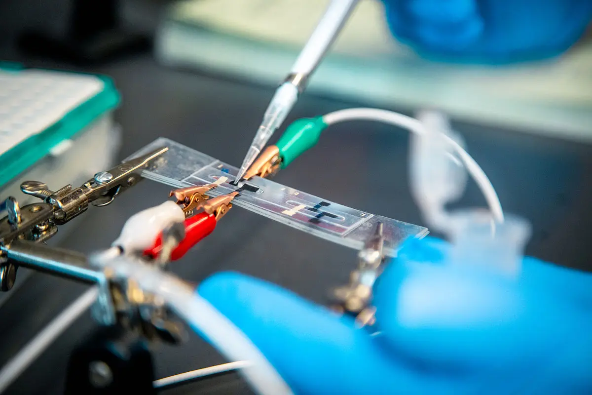 A pipette delivers a small amount of liquid to an electronic circuit embedded on a microscope slide