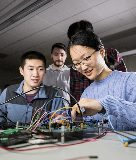 Four students gathered around a circuit board.