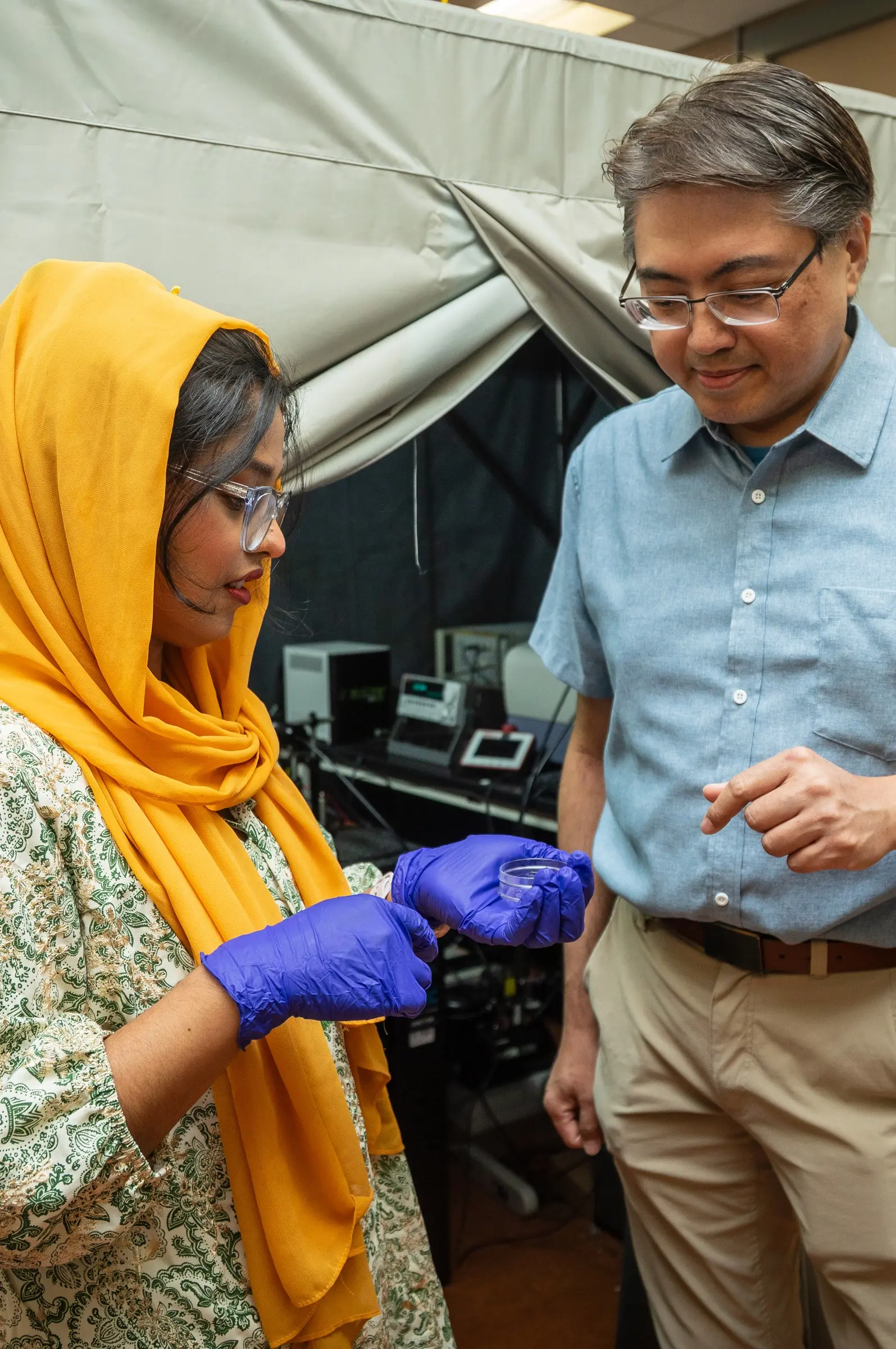 Two people looking at a small petri dish.