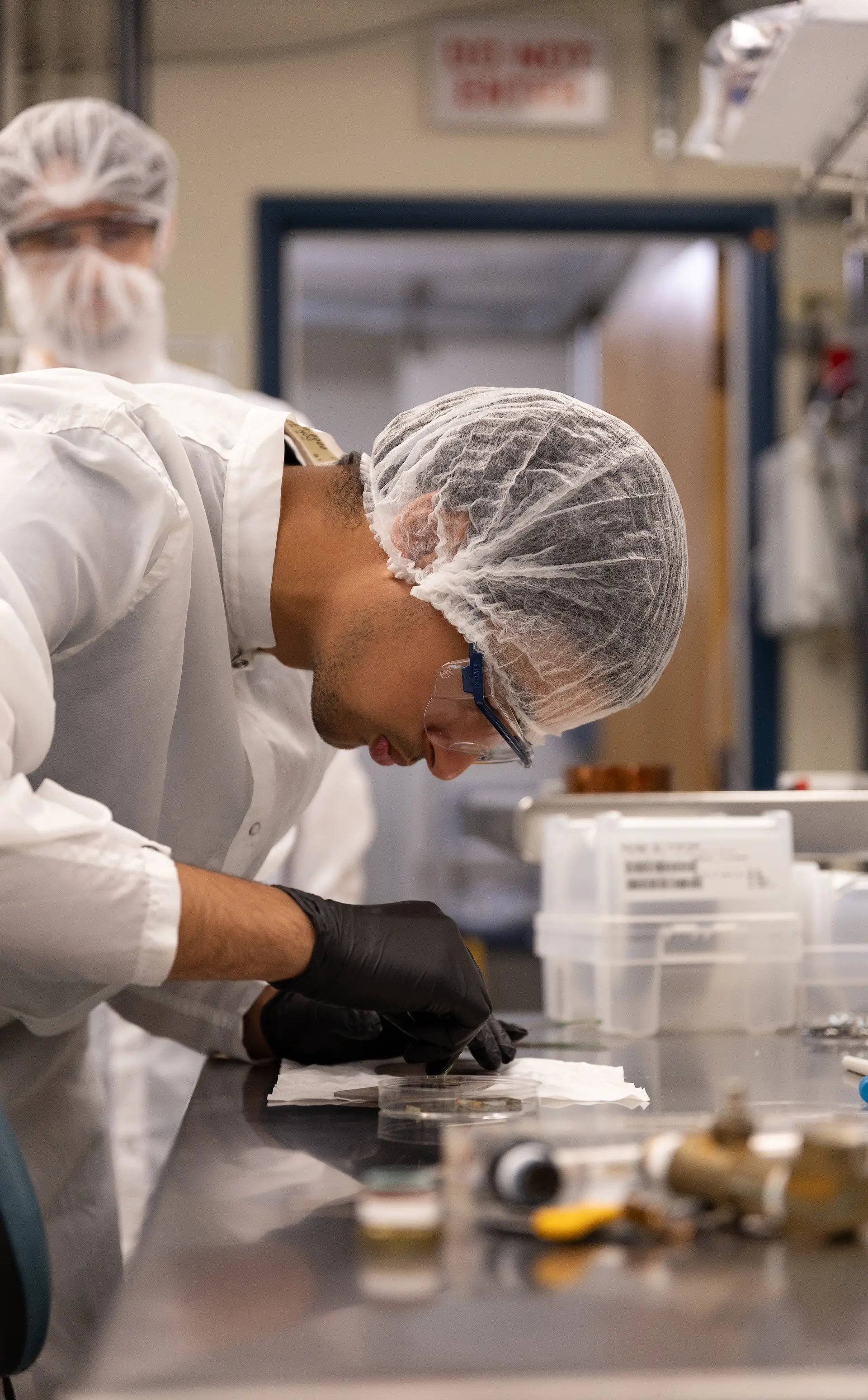 Student wearing protective gear in a lab working on a sample in a petri dish.