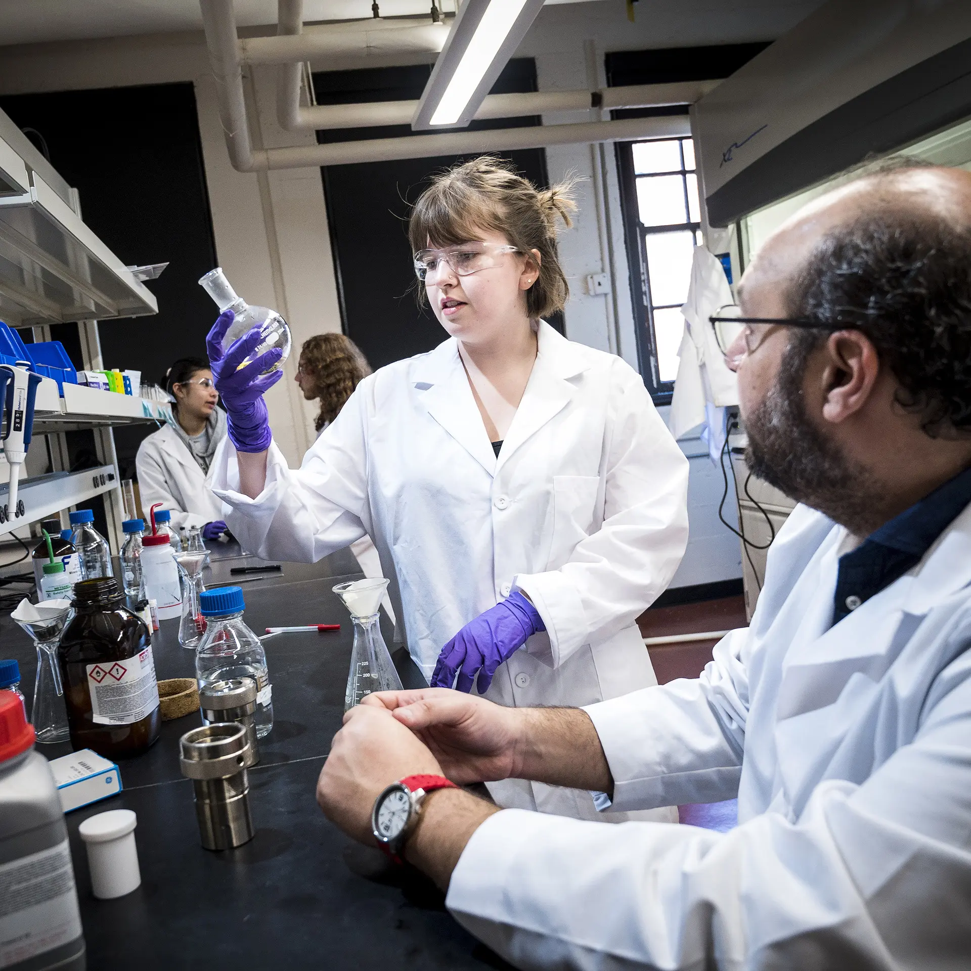 Researchers in a lab handling chemicals in glass vials.