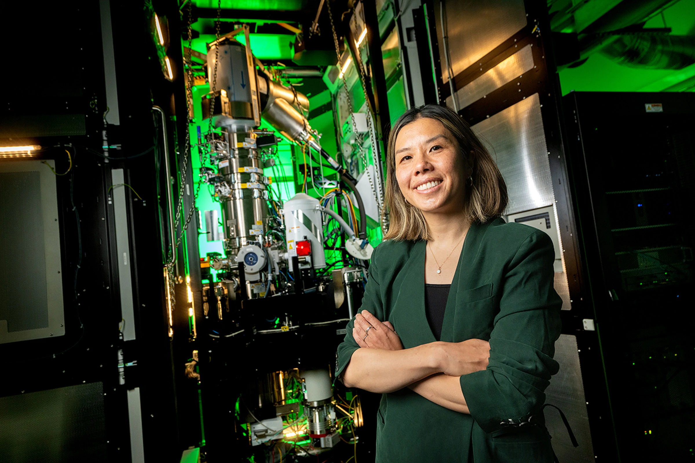 Kayla Nguyen stands in front of advanced laboratory equipment with panels and cables.