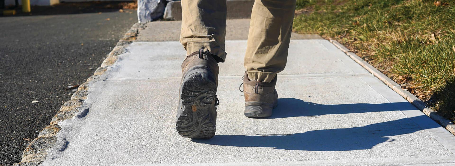 A pair of legs walking on dry concrete.