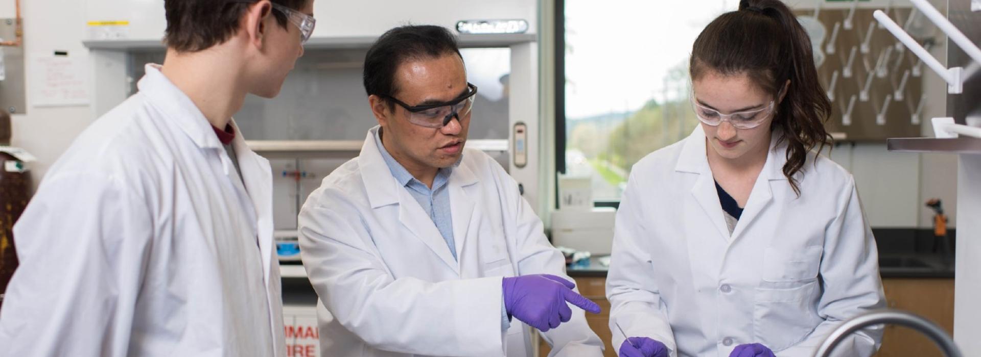 Professor guiding two students in lab uniform