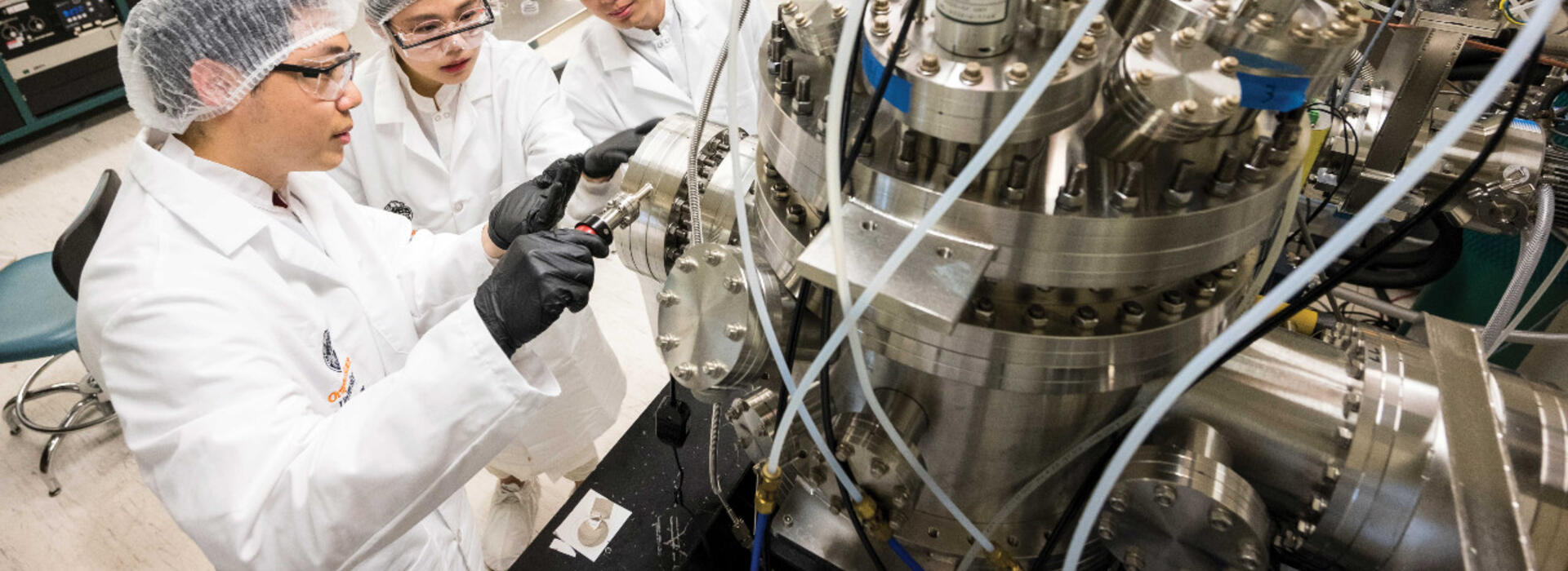 Three students in lab uniform working on a machine.