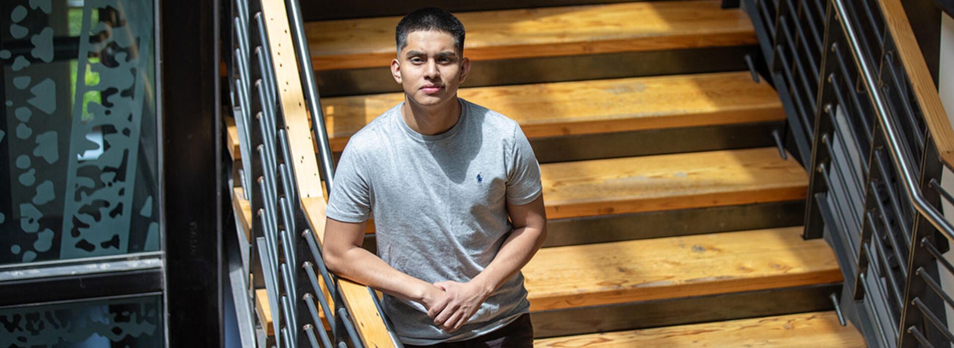 A person stands on wooden stairs within a large atrium and looks up at the camera.