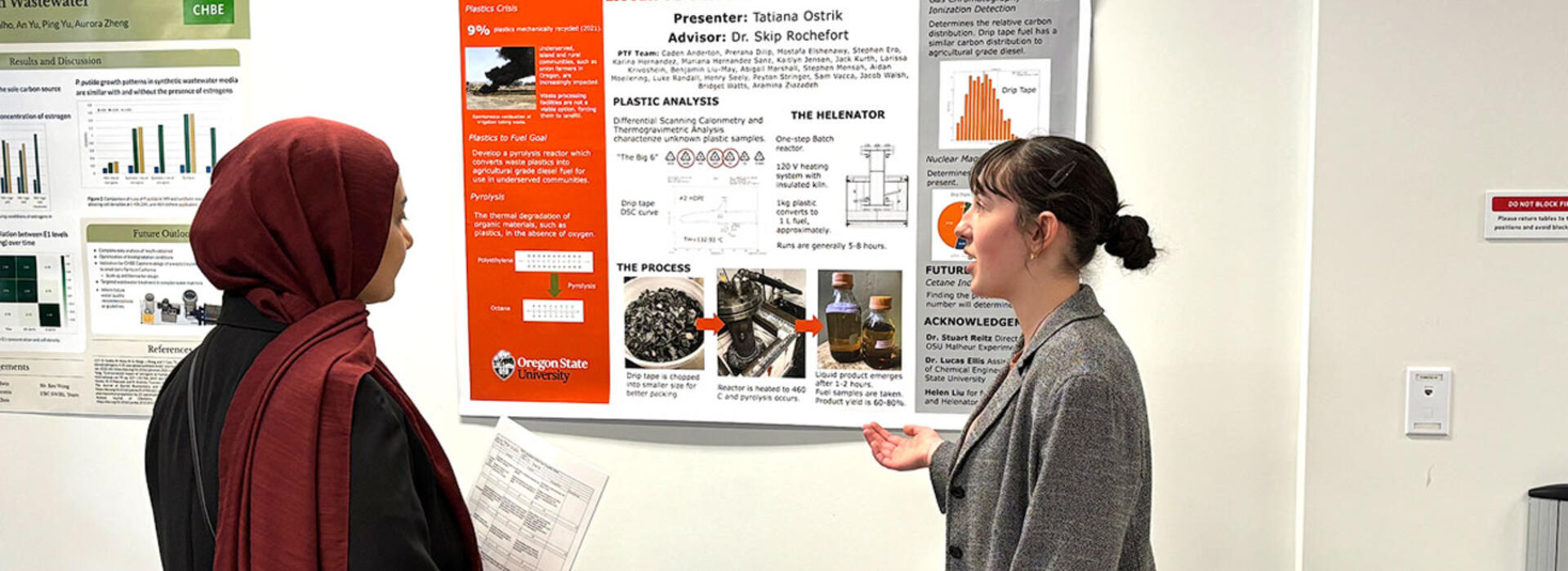 A woman presents a poster to a fellow student during a tabling event.