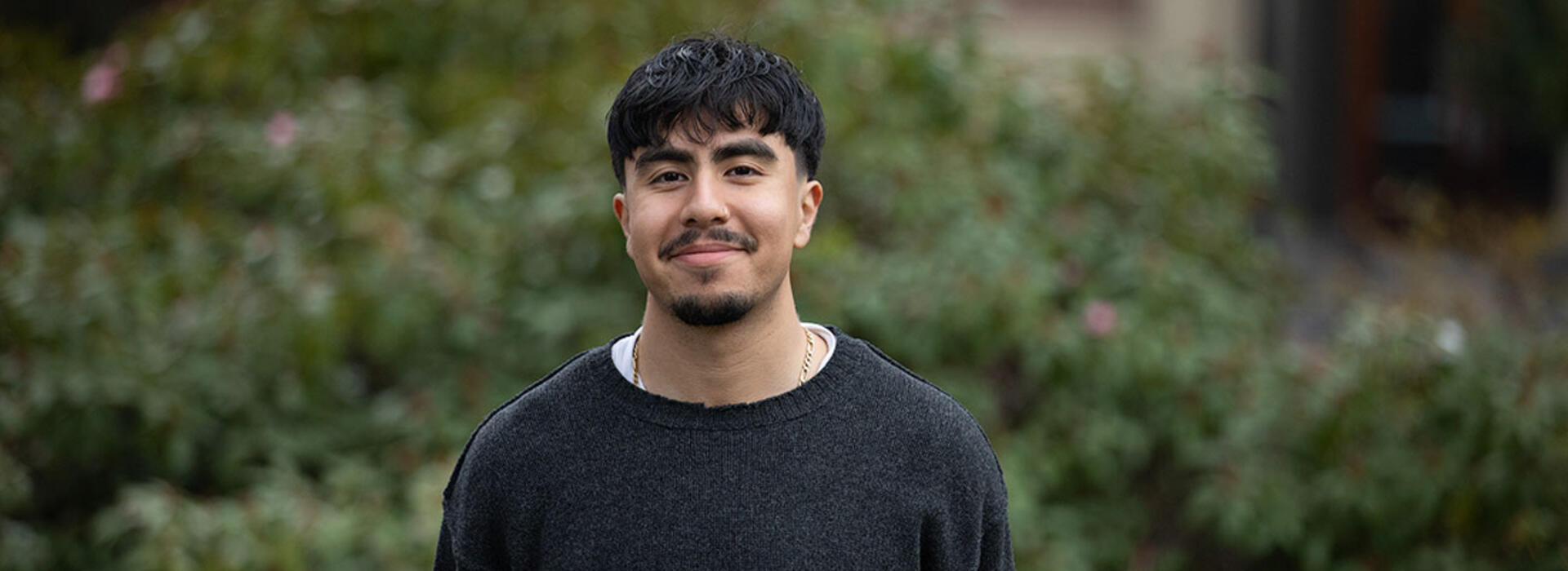 A person stands outdoors with green vegetation in the background.