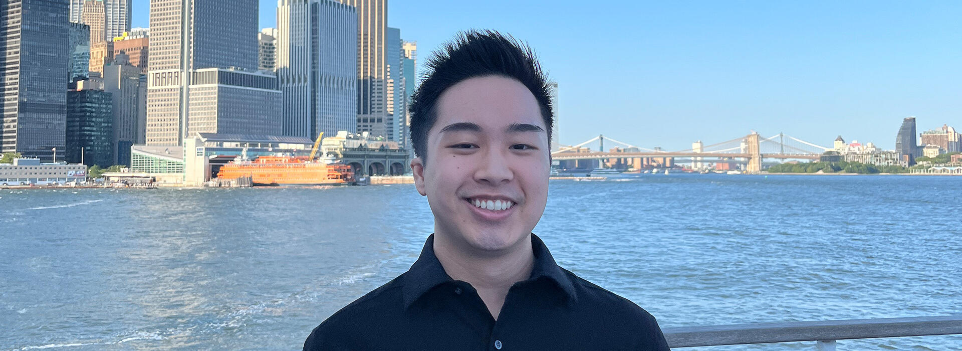 Chris Ho stands on a boat with the New York City skyline behind him.