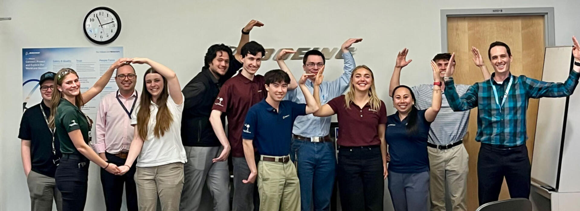 MECOP students in a conference room with the Boeing logo on the wall behind them and form the letters OSU with their arms.