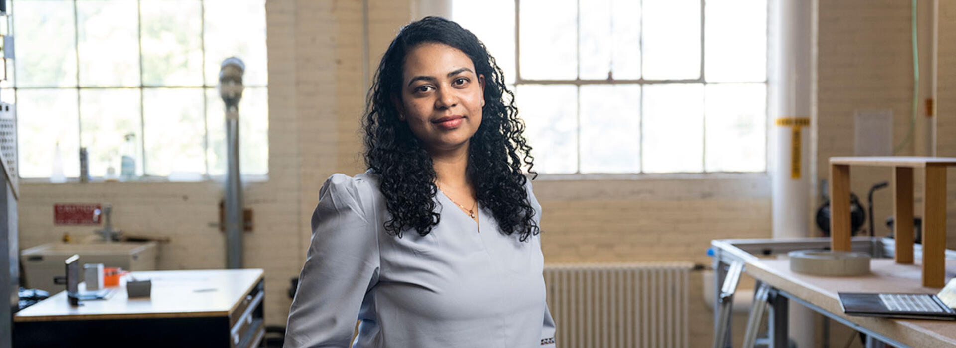 Sandhya Saisubramanian stands in a lab with windows behind her and workbenches and hardware in the background. 