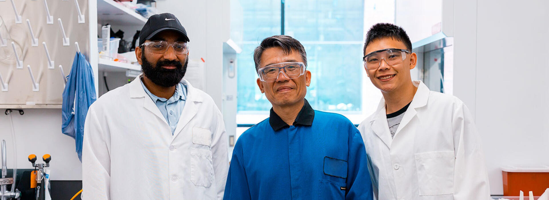 Venkata Vinay Doddapaneni, Chih-hung Chang, and Alvin Chang stand in a lab in Johnson Hall wearing lab coats and protective eyeglasses.