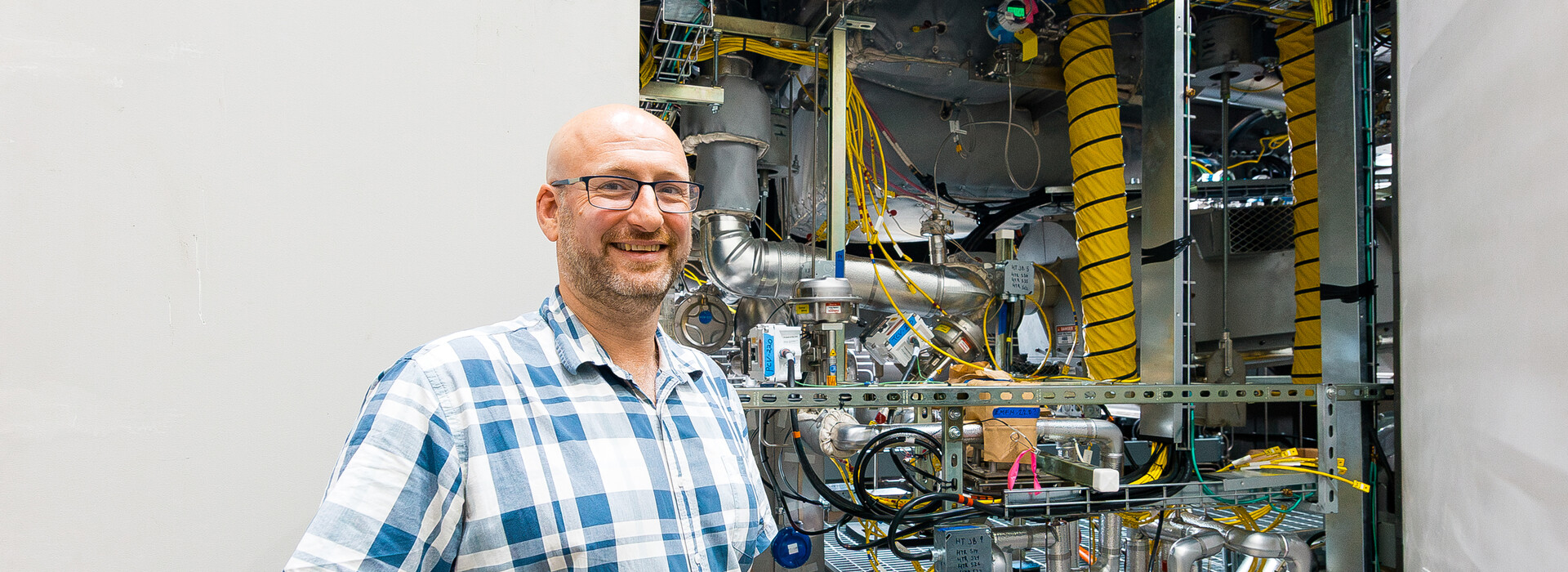 Guillaume Mignot stands outside beside a large instrument filled with pipes, cables, valves, and metal components.