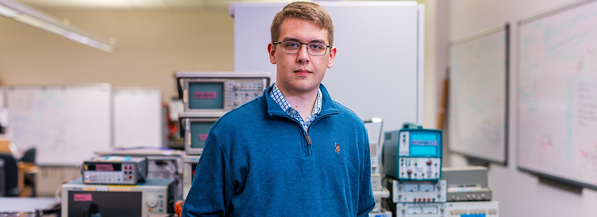 John Fletcher stands inside of a laboratory with testing equipment, workstations, and whiteboards in the background.