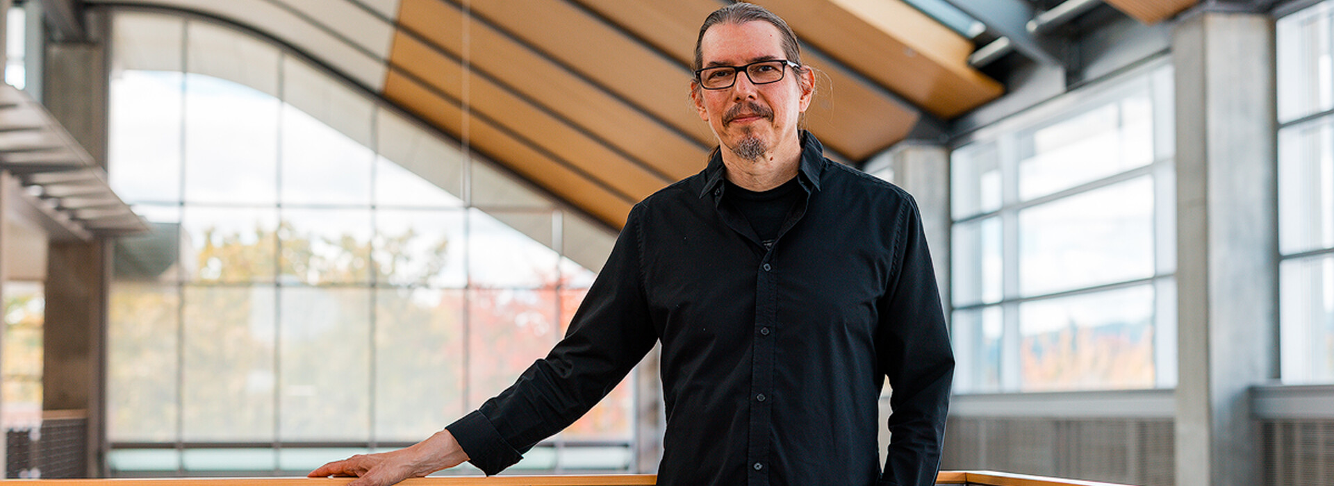 Renato Figueiredo stands inside a modern building and leans against a railing with large windows and columns in the background.