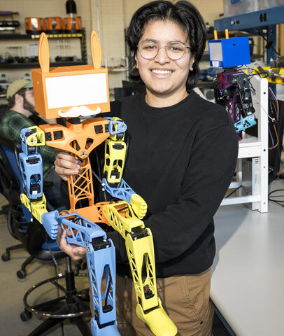 Student stands next to colorful humanoid robot. 