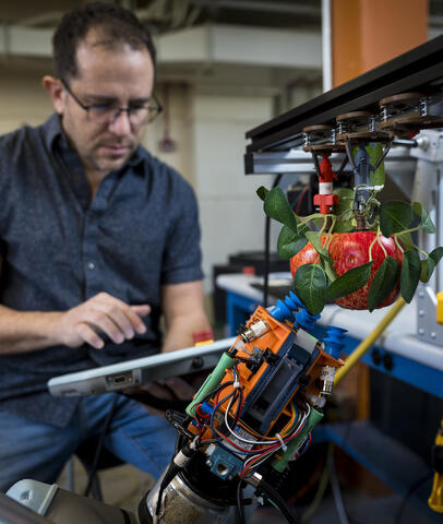 A researcher interacts with device in front of robotic arm holding an apple.