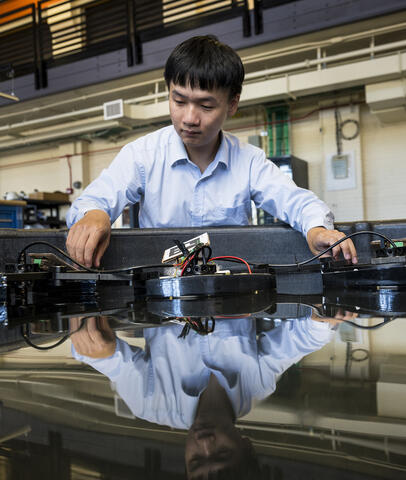 A researcher works on a soft robotics project in a lab, with the scene reflected on a glossy black surface.