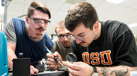 Three students soldering a circuit board. 