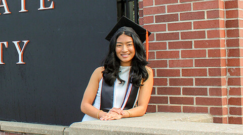 Megan Thomas wearing gradation cap and stole standing next to sign that says Oregon State University.