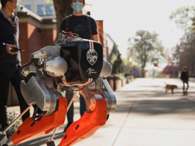 Students near a robot with two legs and the Oregon State University logo.