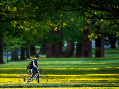 A student with a bicycle walking alongside the trees at Oregon State University Campus.