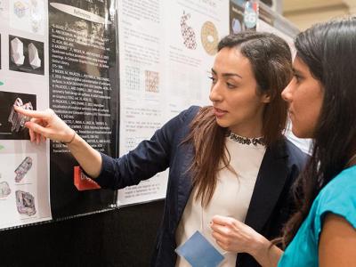 Two students in front of a flyer with pictures.