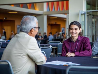 Two people talking to each other while sitting at a table.