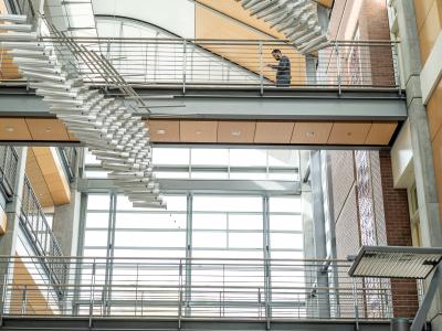 One person walks across the third floor walkway in the atrium of Kelley Engineering. 
