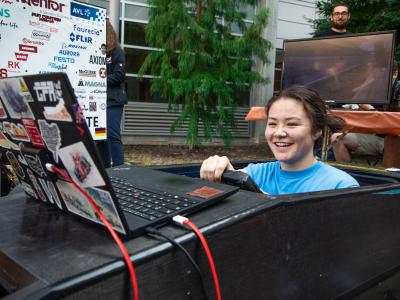 Student sits in replica vehicle outdoors at club event.