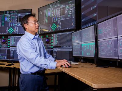 Faculty member Qiao Wu in front of screens at the NIST facility.