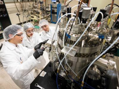 Three students in lab uniform working on a machine.
