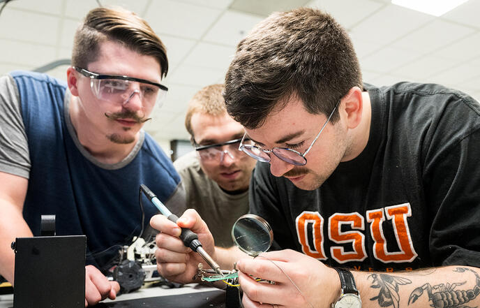 Three students soldering a circuit board.